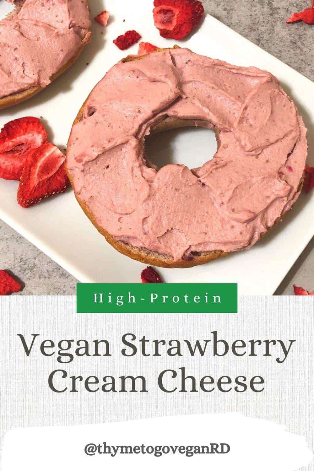 Photo of vegan strawberry cream cheese spread on a bagel on a white plate with freeze-dried strawberries sprinkled around it. Text overlay reads "High protein vegan strawberry cream cheese"