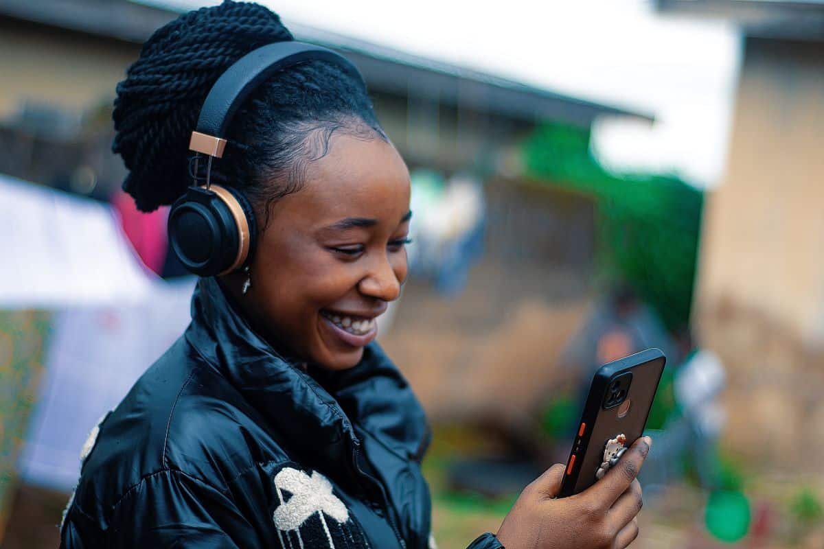 Woman wearing headphones holding mobile phone and smiling