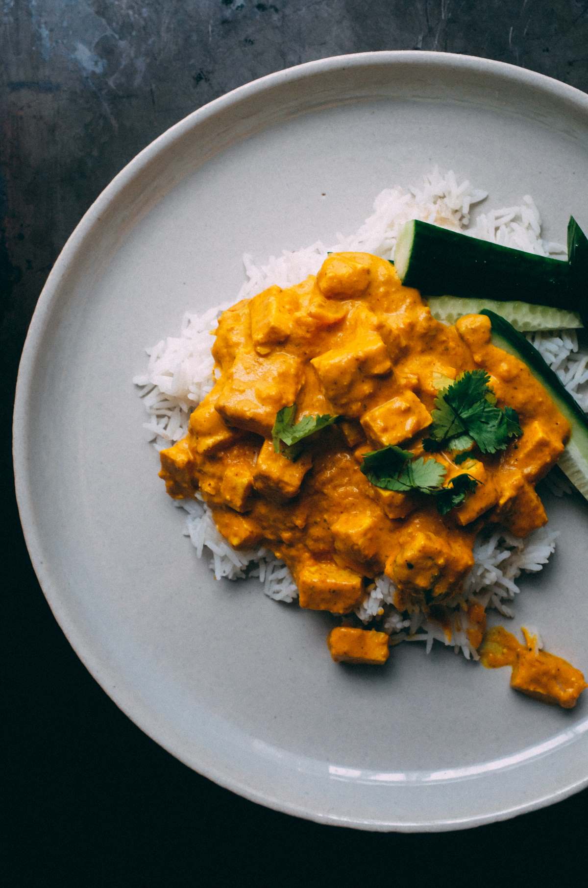 Tofu curry over rice on a white plate and dark gray countertop