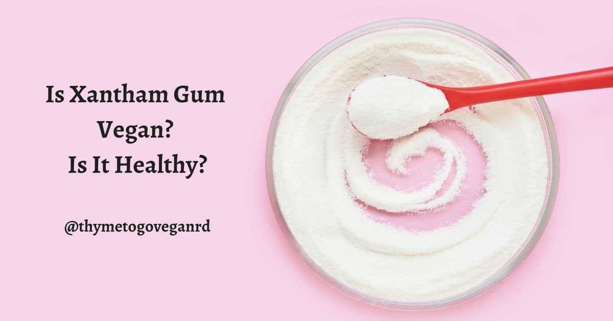 Dish with xanthan gum and a pink spoon on a light pink background with text overlay reading "is xanthan gum vegan? is it healthy? @thymetogoveganRD"